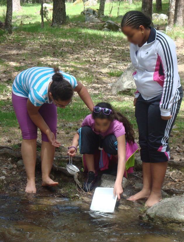Unas alumnas extraen matería orgánica del arroyo con un colador para su posterior análisis